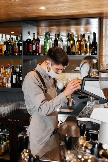 Ein maskierter Barista bereitet an der Bar in einem Café einen exquisiten, köstlichen Kaffee zu Die Arbeit von Restaurants und Cafés während der Pandemie