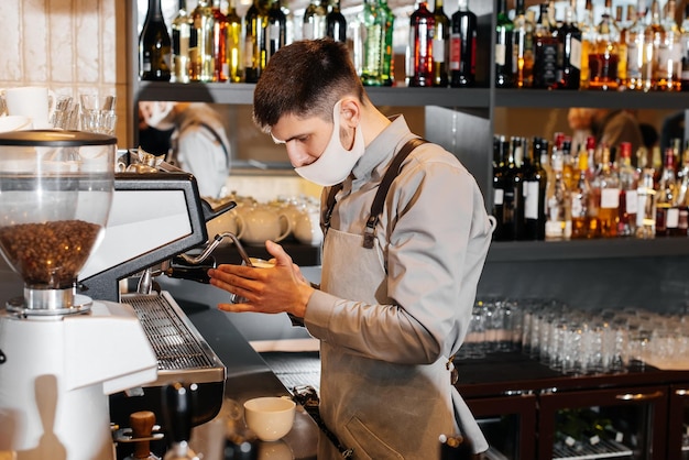 Ein maskierter barista bereitet an der bar in einem café einen exquisiten, köstlichen kaffee zu die arbeit von restaurants und cafés während der pandemie