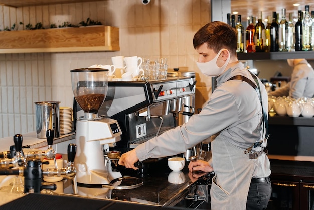 Ein maskierter Barista bereitet an der Bar in einem Café einen exquisiten, köstlichen Kaffee zu. Die Arbeit von Restaurants und Cafés während der Pandemie.
