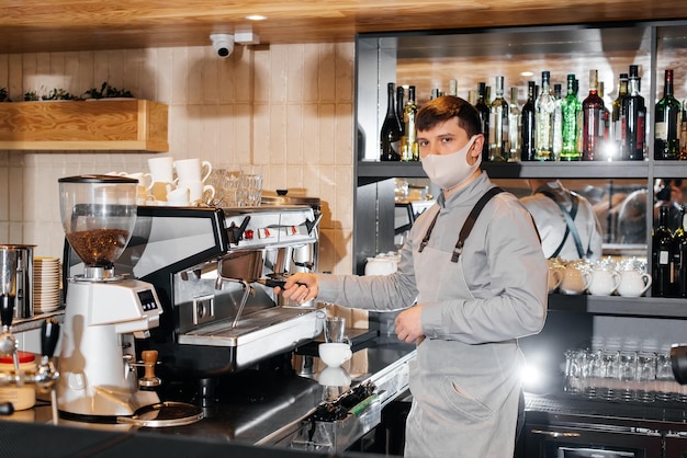 Ein maskierter Barista bereitet an der Bar in einem Café einen exquisiten, köstlichen Kaffee zu Die Arbeit von Restaurants und Cafés während der Pandemie