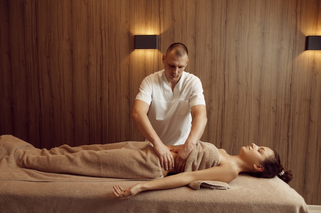 Ein Masseur verwöhnt den Bauch der jungen Frau im Handtuch, professionelle Massage. Massage und Entspannung, Körper- und Hautpflege. Attraktive Dame im Spa-Salon