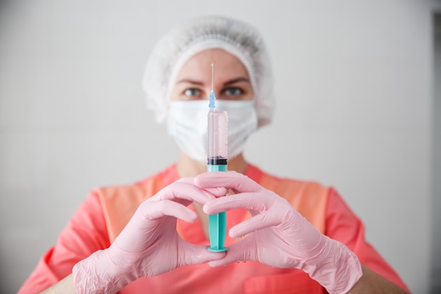 Ein medizinischer Arbeiter in einem rosa Gewand, einer weißen Mütze und rosa Handschuhen hält eine Spritze mit einem Impfstoff