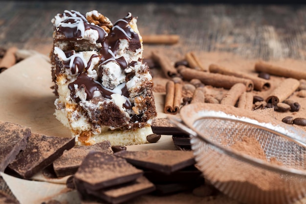 Ein mehrschichtiger Kuchen aus Schokoladen- und Sahnetorten in chaotischer Anordnung im Kuchen, viel Schokoladen-Zimt und Kakaopulver um den Kuchen herum verstreut