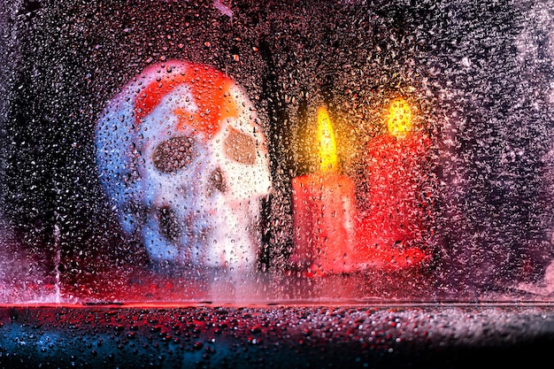 Ein menschlicher Schädelkopf und eine Kerze mit Wassertropfen im Fenster vor dunklem Hintergrund. Gruseliges Totenkopf-Halloween-Konzept