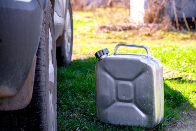 Ein Metallkanister mit Benzin steht im Gras neben dem Auto.