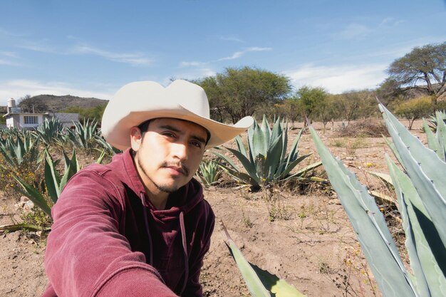 Foto ein mexikanischer latino-mann mit hut arbeitet auf dem feld, umgeben von pulque- und tequila-agaven