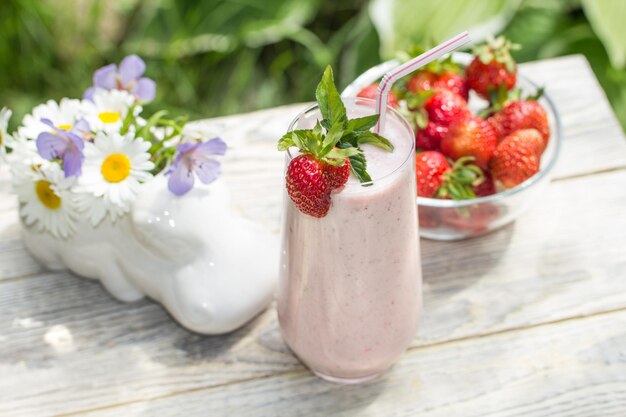 Ein Milchshake mit Erdbeeren steht vor einem hellen Holzhintergrund