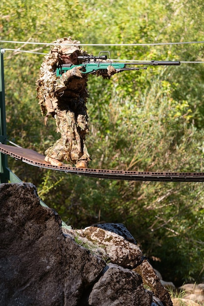 Foto ein militärmann oder airsoft-spieler in einem tarnanzug, der sich über die seilbrücke schleicht und von einem scharfschützengewehr zur seite oder zum ziel zielt.