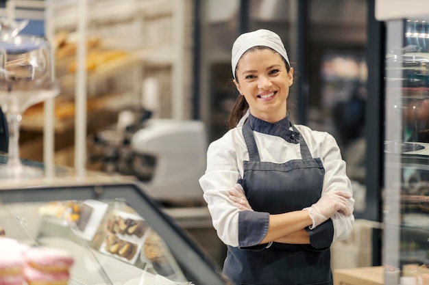 Ein Mitarbeiter der Bäckereiabteilung steht mit verschränkten Armen im Supermarkt und lächelt in die Kamera