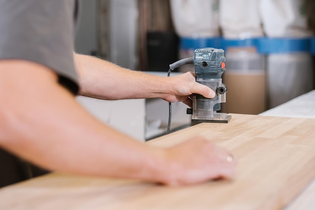 Ein Mitarbeiter einer Möbelfabrik schleift eine Holzoberfläche mit einer Schleifmaschine