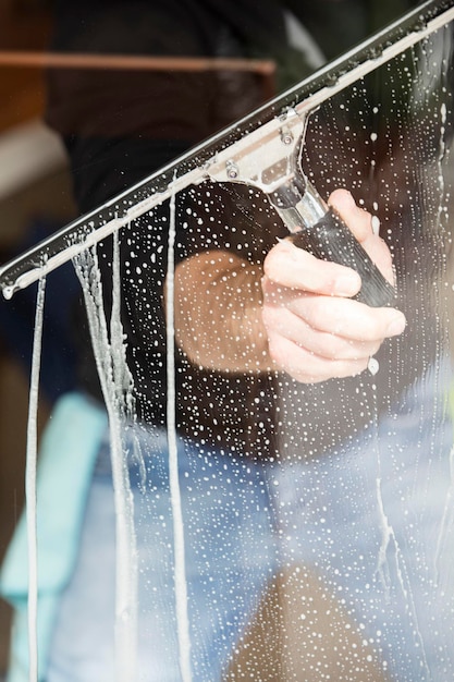 Ein Mitarbeiter eines professionellen Reinigungsdienstes in Overalls wäscht das Glas der Fenster der Fassade des Gebäudes Vitrinenreinigung für Geschäfte und Unternehmen