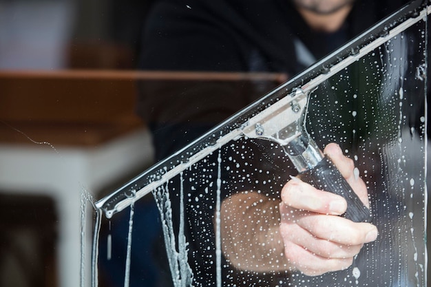 Ein Mitarbeiter eines professionellen Reinigungsdienstes in Overalls wäscht das Glas der Fenster der Fassade des Gebäudes Vitrinenreinigung für Geschäfte und Unternehmen