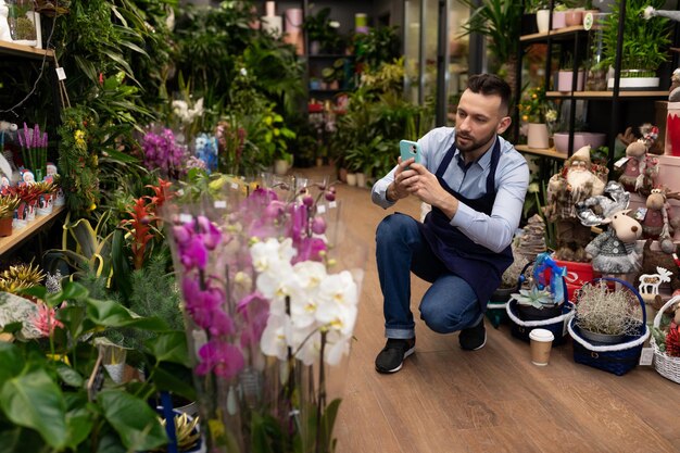 Ein Mitarbeiter in einem Blumenladen macht am Telefon ein Foto von Blumensträußen