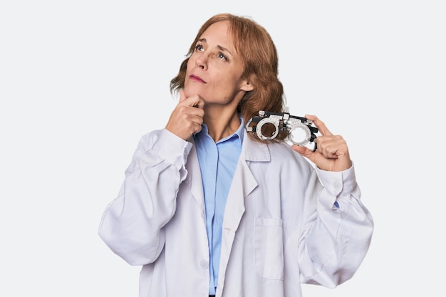 Ein mittelalterlicher kaukasischer Optometrist im Studio, der mit zweifelhaftem und skeptischem Gesichtsausdruck seitwärts schaut