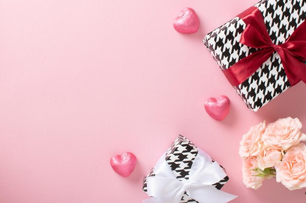 Ein Modell eines Valentinstagsbanners mit einer Geschenkbox, herzförmigen Bonbons und einem Rosenstrauß auf rosafarbenem Hintergrund