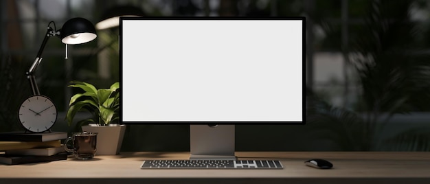 Ein moderner Heimbüro-Schreibtisch bei Nacht mit einem Whitescreen-Computer-Mockup mit schwachem Licht von einer Tischlampe