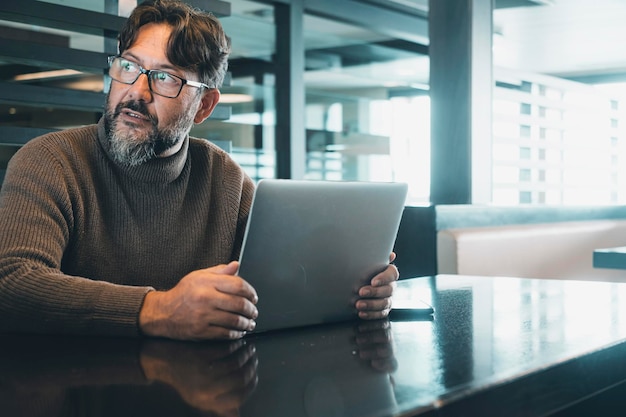 Ein moderner Mann, der an einem Laptop am Schreibtisch in einem leeren Büro oder Coworking Space mit Licht im Hintergrund arbeitet. Angst um ein Sicherheitskonto. Intelligente Lifestyle-Menschen mit Online-Job. Allein auf seiner Seite