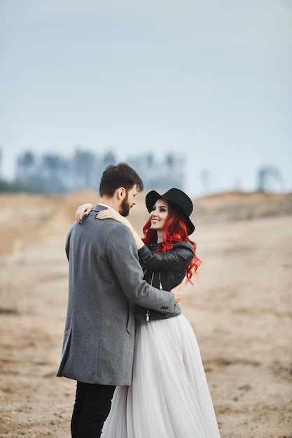 Ein modisches Brautpaar posiert im Freien, ein stylischer bärtiger Mann und seine rothaarige Freundin i...
