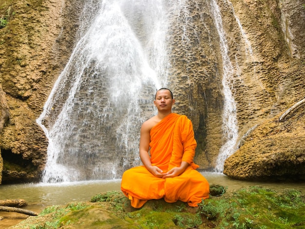 Foto ein mönch meditiert, während er gegen einen wasserfall sitzt