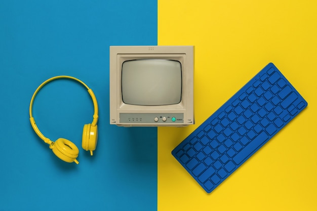 Ein Monitor, eine blaue Tastatur und gelbe Kopfhörer auf gelbem und blauem Hintergrund. Vintage-Ausrüstung. Flach liegen.