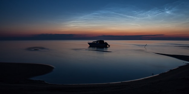 Ein Motorboot auf dem stillen Wasser des Sees unter silbernen Wolken in der Sommernacht