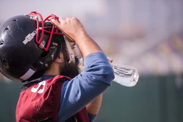 Ein müder American-Football-Spieler, der Wasser trinkt, während er sich nach dem harten Training auf dem Feld ausruht