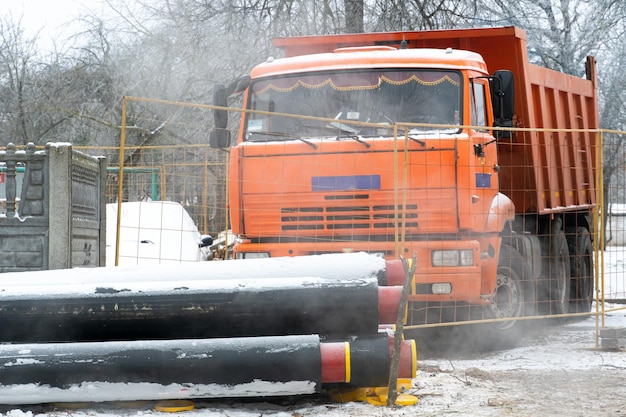 Ein Muldenkipper mit roter Kabine steht im Winter auf einer Baustelle in der Nähe von neuen Wasserleitungen Ein Straßenmuldenkipper für den Transport von Erde