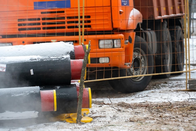 Ein Muldenkipper mit roter Kabine steht im Winter auf einer Baustelle in der Nähe von neuen Wasserleitungen Ein Straßenmuldenkipper für den Transport von Erde