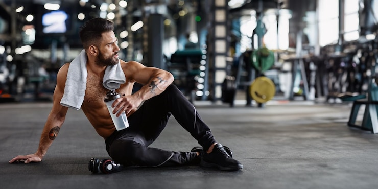 Foto ein muskulöser mann in sportbekleidung sitzt auf dem fitnessboden und macht nach einem training eine pause und hält ein wasser in der hand