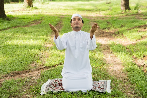Ein muslimischer Mann betet zu Allah, dem Gott des Islam, auf einer grünen Wiese.