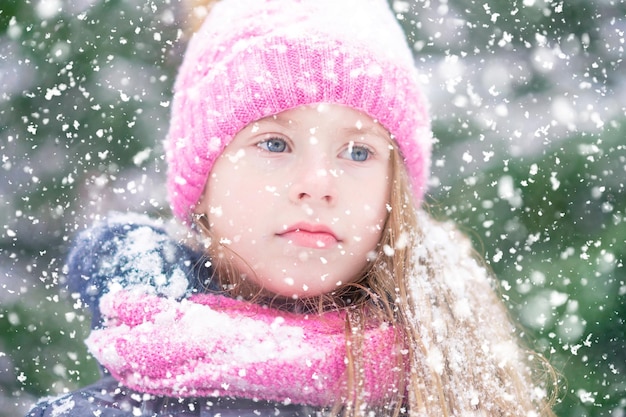Ein nachdenkliches blondes Mädchen mit rosafarbenem Hut bei Schneewetter