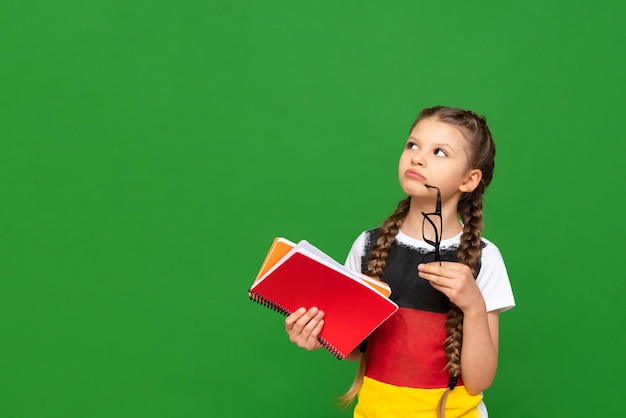 Ein nachdenkliches Kind mit deutscher Flagge und einem Notizbuch in den Händen auf grün isoliertem Hintergrund Deutschkurse für Schulkinder