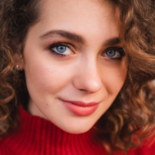 Ein Nahaufnahmeporträt einer jungen Frau mit lockigem braunem Haar und durchdringenden blauen Augen, die einen Pullover trägt
