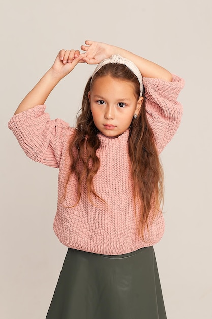 Ein Nahaufnahmeporträt eines ernsten kleinen schönen Mädchens mit langen Haaren, das Kind schaut mit ernstem Blick in die Kamera und hob die Hände über den Kopf. stilvolles Porträt eines Kindes.