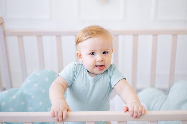Foto ein nahaufnahmeporträt eines kleinen blonden babys ein baby mit blauen augen zeigt seine zunge sitzend in einer krippe lustiger kleiner junge neckt