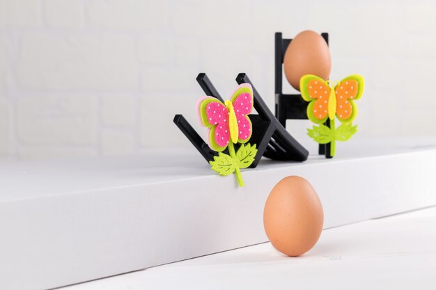 Ein natürliches Ei auf weißem Hintergrund und zwei schwarze Stuhl mit Ei und Ostern Blumendekoration. Minimale Osterkonzeptidee.