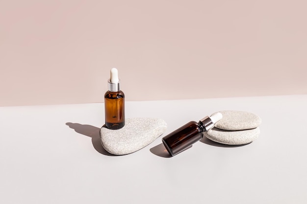 Ein natürliches Schönheitsproduktserum oder Bio-Selbstpflegeöl in zwei Kosmetikflaschen mit einer Pipette zwischen ovalen grauen Steinen