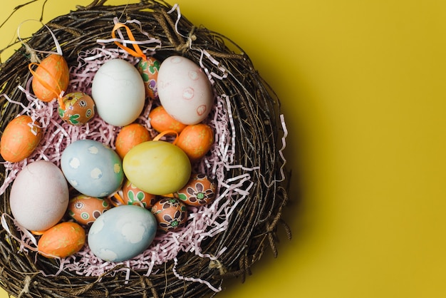 Ein Nest aus Zweigen und Heu und ein rosa Papierfüller mit pastellfarbenen Ostereiern