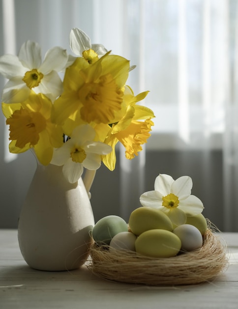 Foto ein nest mit eiern in sanften pastellfarben und eine vase mit narzissen auf einem tisch am fenster