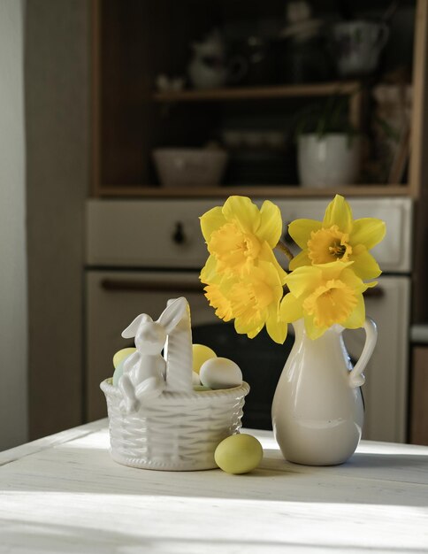 Ein Nest mit Eiern in zarten Pastellfarben und eine Vase mit Narzissen auf dem Küchentisch