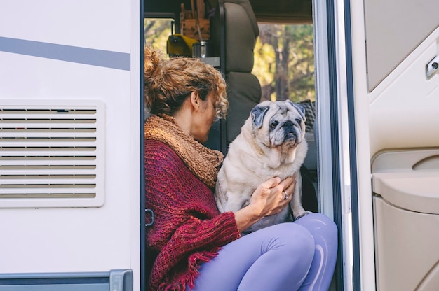 Ein netzunabhängiger Lebensstil mit einer Frau und ihrem besten Freundhund, der an der Tür eines modernen Wohnmobils sitzt und sich entspannt. Alternative Vanlife-Menschen und -Tiere Freiheit und Reiseurlaub