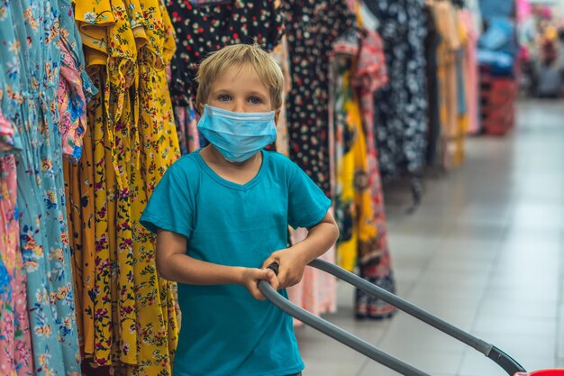 Ein neuer normaler kaukasischer Junge in sanitärer Gesichtsmaske, der im Supermarkt einkauft Kind mit Einkaufskorb Kind mit Schutz vor Coronavirus Sicherheit Gesundheitsschutz während der Covid19-Quarantäne