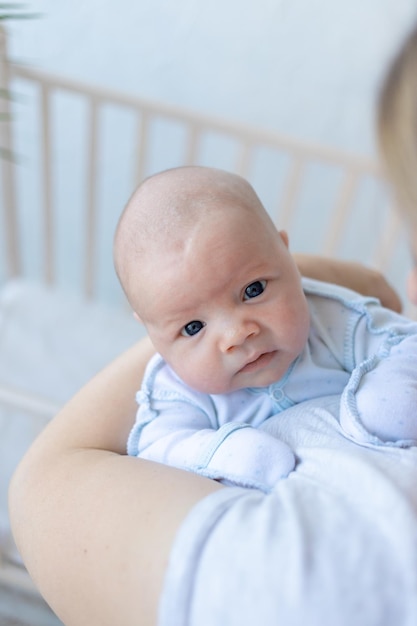 Ein neugeborener Junge in den Armen seiner Mutter in der Nähe der Krippe zu Hause elterliche Liebe und Fürsorge für das Baby in den ersten Tagen nach der Geburt