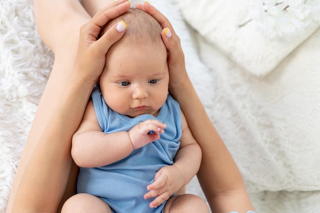 Ein neugeborenes Baby in den Armen meiner Mutter auf dem Bett zu Hause, sanfte Umarmung der Mutter