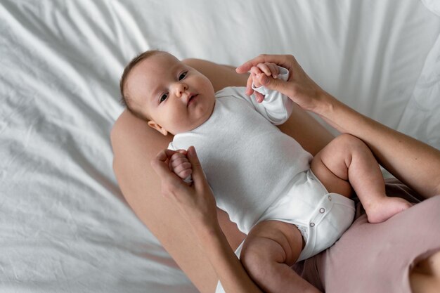 Ein neugeborenes Baby liegt auf einem weißen Laken auf dem Bett im Schlafzimmer. Mamas Hände halten die Finger ihrer Tochter.