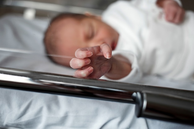 Ein Neugeborenes liegt in einer Kiste im Krankenhaus. Kleines Baby zeigt dem Fotografen seine Hand.