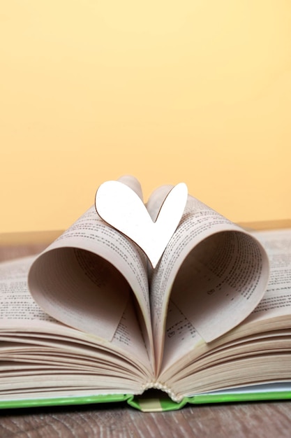 Ein offenes Buch mit einem hölzernen Herzen auf dem Tisch Konzept Liebe zum Lesen von Büchern Bibliotheksbildung Close up Copy Space Hochformat
