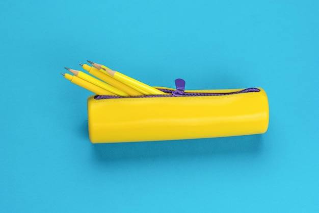 Ein offenes gelbes Federmäppchen mit hervorstehenden Stiften auf blauem Hintergrund Das Mindestkonzept zur Aufbewahrung von Schulmaterial Flach lag