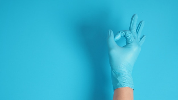 Ein Okay-Handzeichen mit Handschuhen in der rechten Hand auf blauem Hintergrund