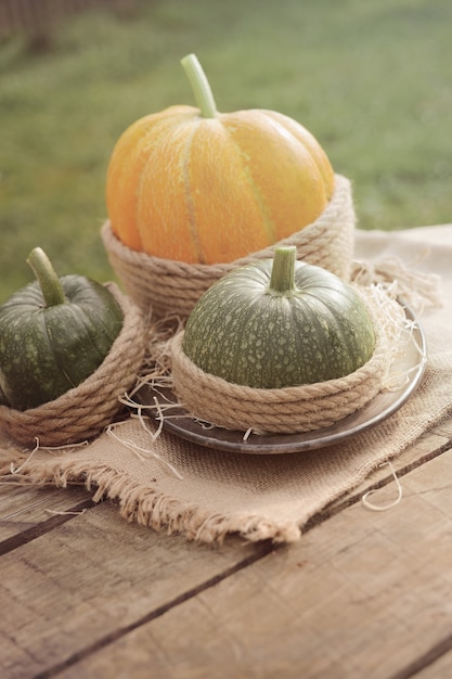 Ein orangefarbener Kürbis und zwei grüne Kürbisse auf dem Holztisch verzierten Sackleinen und Seil. Draußen.